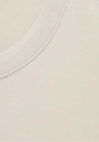 Jasno beżowa bawełniana tkanina z okrągłym dekoltem i delikatną fakturą, o gładkim wykończeniu i drobnych detalach szwów wokół kołnierza.