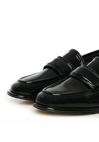 Zwarte gepatineerde leren loafers met een ronde neus en een decoratieve band over de wreef. Kenmerken een gladde, glanzende textuur en geen zichtbare hardware.