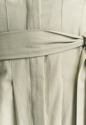 Lichtgrijze katoenen jurk met plooien en een geknoopte tailleband. Soepele textuur met zichtbare stikseldetails overal.