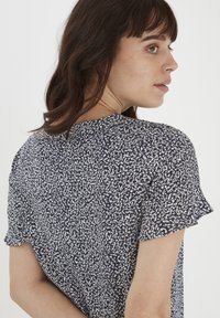 Blusa blu navy con motivo puntinato bianco, maniche corte a volant e scollatura tonda. Tessuto leggero con una texture morbida.