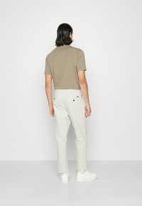 Ljusbrun kortärmad skjorta i kombination med vita smalbenade byxor och vita sneakers. Enfärgad textur, minimalistisk design, bakifrån.