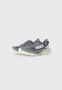 HOKA Laufschuhe mit einem grau-weißen gesprenkelten Design, einem strukturierten Mesh-Obermaterial, einer dicken weißen Zwischensohle und einer Vibram-Außensohle für Grip.