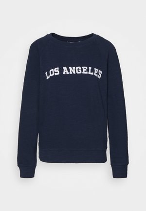 Granatowa bluza z długim rękawem z białym napisem „LOS ANGELES” na klatce piersiowej, okrągłym dekoltem oraz ściągaczami na mankietach i u dołu.