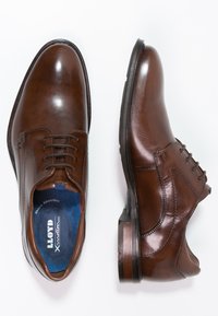 Chaussures en cuir marron avec une finition brillante, design à lacets, doublure intérieure bleue et un talon de hauteur moyenne. Couture détaillée le long des bords.