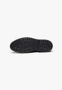 Black rubber shoe sole with deep treads and a rounded shape, featuring prominent textured patterns and a smooth edge.