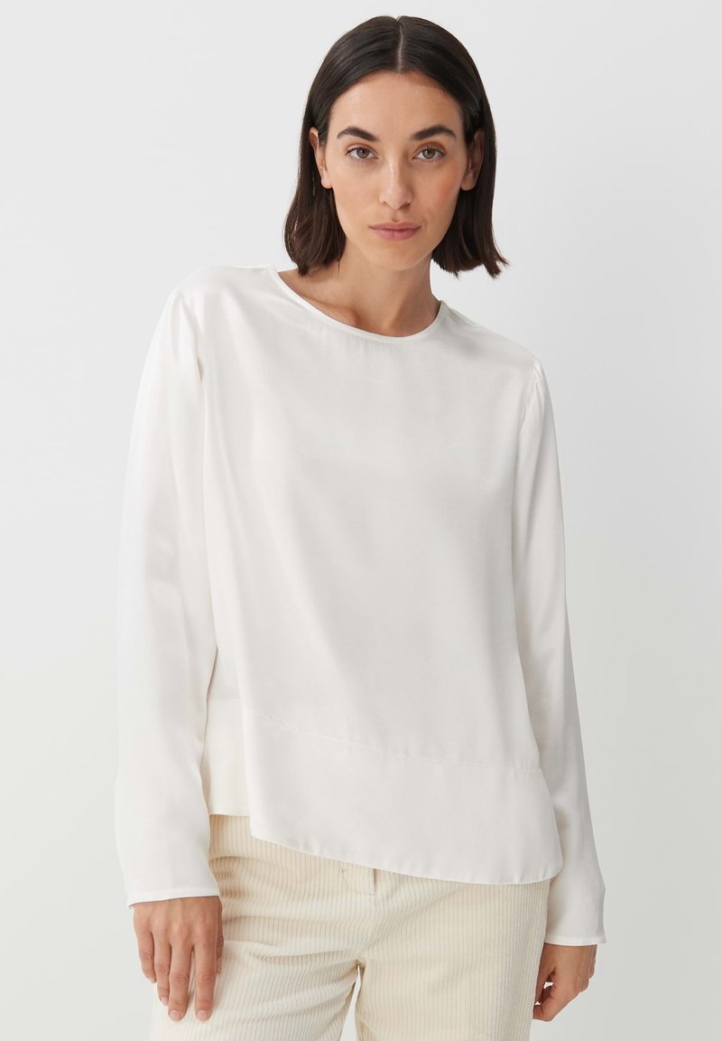 Blusa bianca a maniche lunghe con scollatura rotonda e texture liscia; presenta dettagli di cucitura sottili e una vestibilità comoda.