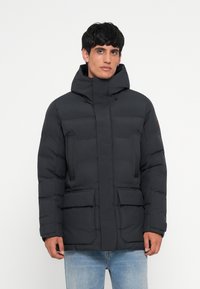 Puffer jacket in dark gray, featuring a high neckline, two front pockets, quilted design, and adjustable hood. Smooth texture.