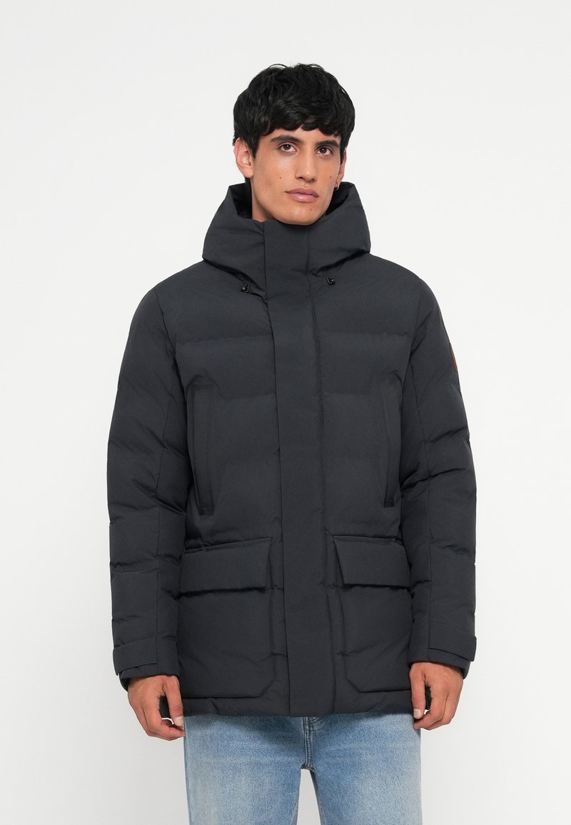 Puffer jacket in dark gray, featuring a high neckline, two front pockets, quilted design, and adjustable hood. Smooth texture.