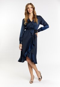 Navy satin jurk met lange mouwen, een v-hals, een strik taille en een gerimpelde zoom. G gedragen met metallic hoge hakken.