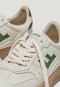 Baskets en cuir blanc avec des accents verts. Présentent une semelle texturée beige, des détails cousus et des lacets plats beiges. Logo sur la languette.