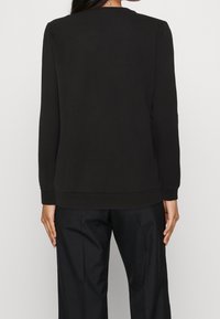 Sudadera negra de manga larga con cuello redondo, puños y dobladillo acanalados, hecha de tela suave, con un corte holgado y diseño minimalista.