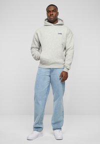 Felpa grigia in pile con tasca a canguro e cappuccio regolabile, abbinata a jeans di denim azzurri e sneakers bianche.