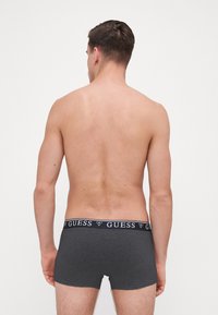 Boxeri gri cu un design ajustat. Banda elastică are logo-ul "GUESS" în alb, material simplu și textură netedă.