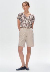 Beżowe spodenki z podwiniętym brzegiem i pasującym paskiem, zestawione z bluzką z krótkim rękawem w kolorze białym, ozdobioną ciemnobrązowym wzorem kwiatowym.