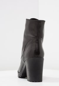Botas de cuero negro hasta el tobillo con un tacón alto y bloque, y suela texturizada. Detalles de costura en la parte trasera y acabado suave en la parte superior.