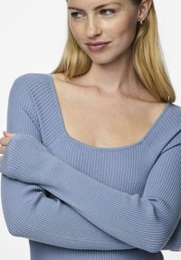 Šviesiai mėlynas banguotas megztinis su kvadratiniu iškirpimu ir ilgomis rankovėmis. Audinys yra minkštas, pasižymintis prigludusia forma ir subtiliomis horizontaliomis juostelėmis.