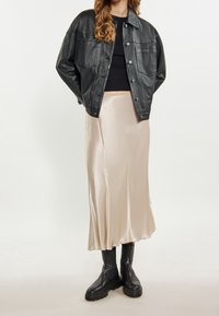 Sort læderjakke, tætsiddende sort top, cremet satin midi-nederdel og kraftige sorte ankelstøvler. Bløde teksturer og kontrasterende farver.