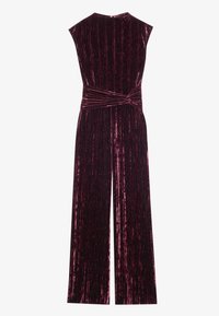 Combinaison en velours bordeaux avec des plis verticaux, des manches courtes et un détail de taille nouée, comportant un pantalon évasé et une texture lisse.