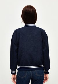 Granatowa kurtka typu bomber z fakturowanym wzorem, białe i granatowe prążkowane mankiety oraz kołnierz, luźny fason i jednolity kolor.