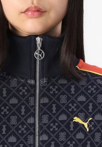 Navy zip-up jacket with high collar, patterned fabric featuring gray graphics, and yellow Puma logo on the chest. Silver zipper hardware.