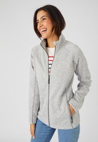 Giacca grigia chiara con zip, dotata di un colletto alto e realizzata in un morbido tessuto texturizzato. Presenta tasche laterali e dettagli con zip grigia a contrasto.