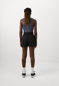 Mustad mustad sportlikud lühikesed püksid, millel on lai elastne vöökoht, koos tumeda, tihedalt istuva tanktopiga. Materjal näib sujuv ja kerge.
