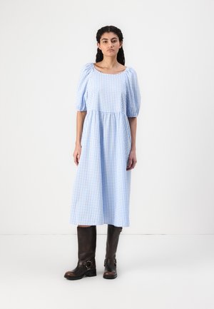 Blå og hvit gingham midi-kjole med puffede ermer og samlet midje, kombinert med knelange brune skinnstøvler med spenner.