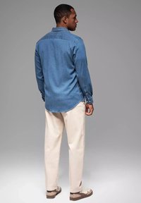 Jeanshemd in Hellblau mit klassischem Kragen, geknöpften Manschetten und abgerundetem Saum. Kombiniert mit cremefarbenen Hosen und braunen Schuhen.