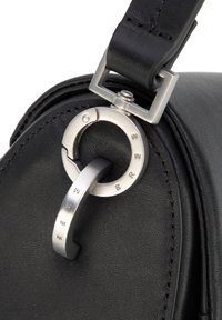 Bolso de cuero negro con un detalle circular de herrajes plateados con letras grabadas, conectado por una correa elegante para un cierre seguro.