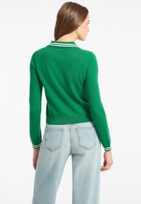 Zielony sweter wykonany na drutach z kołnierzykiem, ozdobiony białymi paskami, w zestawie z jasnoniebieskimi jeansami podwyższonym stanem. Miękka faktura i dopasowany krój.