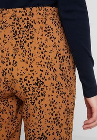 Hnědé kalhoty s leopardím vzorem v černé barvě. Pas je elastický a materiál vypadá texturovaně a lehce.