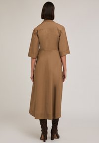 Abito camicia midi marrone con maniche corte, colletto e silhouette dritta. Indossato con stivali con tacco a stampa serpente al ginocchio.