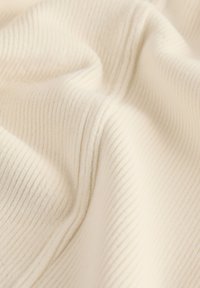 Tessuto a coste di colore crema con una consistenza morbida, caratterizzato da strisce verticali sottili. Il materiale appare flessibile e liscio.