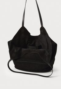 Sac tote en suède noir avec double anses supérieures, texture douce et grand compartiment principal ouvert avec poches intérieures. Détail de couture visible.