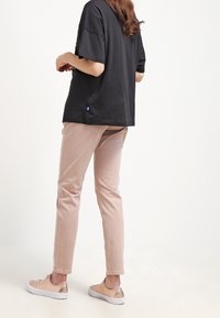 Svart kortärmad skjorta, ljusrosa slim-fit byxor och beige sneakers. Slät tyg med enkel design och inga framträdande mönster eller detaljer.