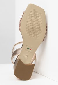 Sandalo beige con tomaia in pelle liscia, tacco flat e suola in gomma tassellata, con decorazioni sulle cinghie. Taglia 37.