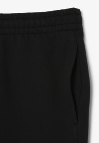 Zwarte sweatpants van een zachte, textuurstof met een elastische tailleband en zijzakken. Eenvoudig ontwerp, zonder patronen of accenten.