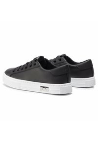 Black leather sneakers with white rubber soles, round toe, flat lace-up design, and metal logo detail on the side. Smooth texture.