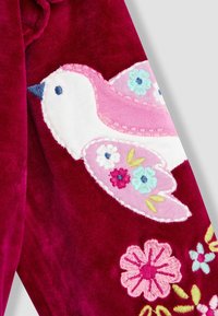 Tessuto di velluto cremisi con un uccello ricamato in rosa e bianco, accentuato da colorati motivi floreali in tonalità pastello.