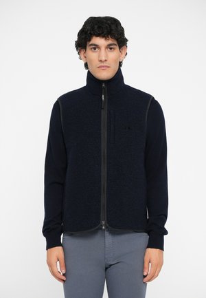 Gilet en polaire zippé de couleur bleu marine foncé avec des manches longues. Doté d'un tissu texturé, d'un col montant et de panneaux latéraux contrastés.