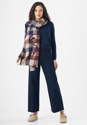 Écharpe à carreaux en crème, marine et bordeaux avec des bords frangés ; associée à un pull ajusté marine et à un jean en denim foncé à jambes larges.