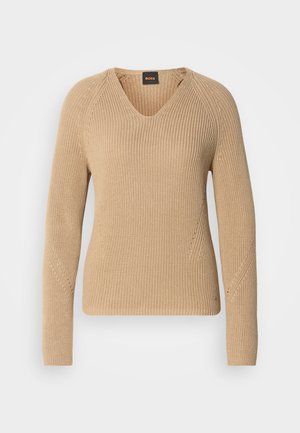 Beige stickad tröja med V-ringning, långa ärmar och texturerad ribbad design med diagonala sömmar på axlarna.