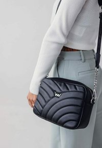 Černá prošívaná crossbody taška se stříbrným kováním, se vzorem vln a detailem loga. Vyrobeno z hladkého materiálu s nastavitelným popruhem.