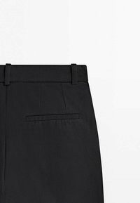 Pantalon noir sur mesure vue arrière montrant la ceinture, les passants et une poche passepoilée simple sur fond blanc.