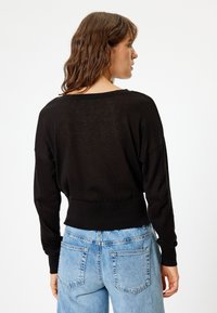 Schwarzer, gestrickter Pullover mit lockerer Passform, weitem Rundhalsausschnitt und geripptem Saum. Kombiniert mit hellblauen, hochtaillierten Jeans mit Gesäßtaschen.