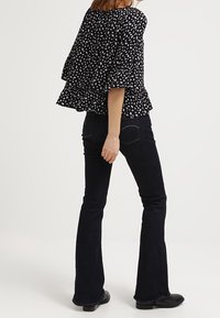 Schwarz-weiß gemusterte Peplum-Bluse mit ausgestelltem Saum, kombiniert mit dunklen Schlagjeans und schwarzen Stiefeletten. Insgesamt ein lässiges Outfit.