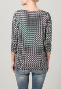 Top con motivo nero e teal con maniche a tre quarti, realizzato in un tessuto morbido e con scollatura arrotondata. Visuale posteriore, indossato con jeans blu chiaro.
