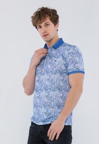 Kortærmet polo shirt i lyseblå med et struktureret mønster. Har en solid mørkeblå krave og kanter, lavet af en blød bomuldsblanding.