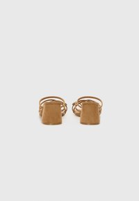 Brune ruskinds hælede sandaler med blokhæle og flere sammenflettede stropper. Glat tekstur med en afrundet tå og minimal detaljering.