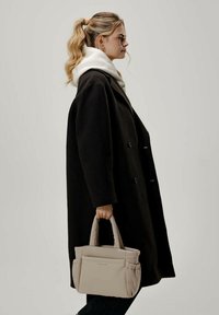 Musta ylisuuri takki, jossa on kaksirivinen muotoilu, yhdistettynä vaaleanbeigeen laukkuun, jossa on tekstuuri pinta ja pehmustetut kahvat.